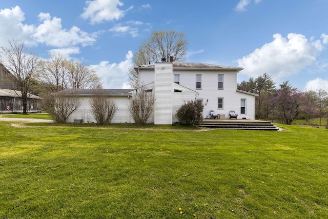 back of house with a chimney, a deck, and a lawn