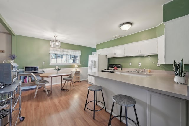 kitchen with range with gas cooktop, a sink, stainless steel microwave, light wood-style floors, and white fridge with ice dispenser
