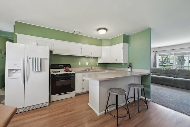 kitchen with range with gas cooktop, white fridge with ice dispenser, a peninsula, white cabinetry, and visible vents