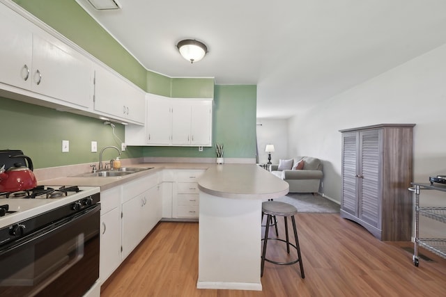 kitchen featuring range with gas stovetop, a sink, light wood-type flooring, a breakfast bar area, and a peninsula