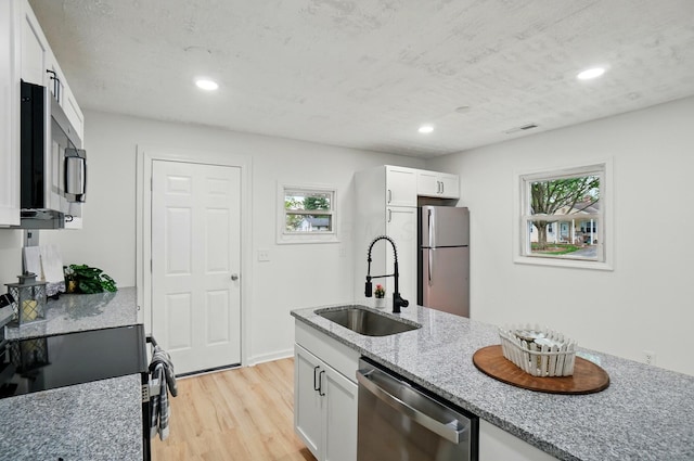 kitchen featuring white cabinets, a sink, light wood-style floors, stainless steel appliances, and visible vents