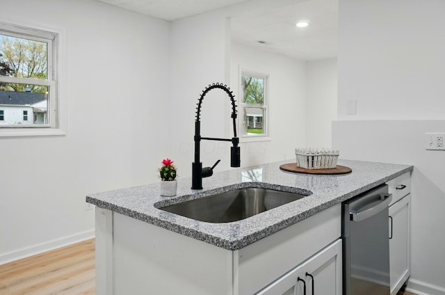 kitchen with light stone countertops, baseboards, a sink, light wood-style flooring, and dishwasher