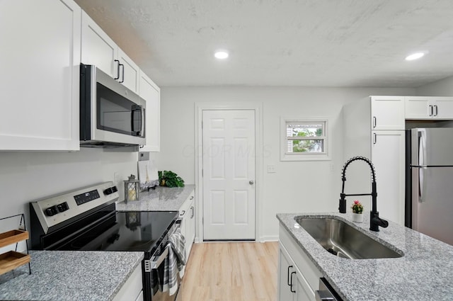kitchen with light stone countertops, white cabinetry, a sink, stainless steel appliances, and light wood-style flooring