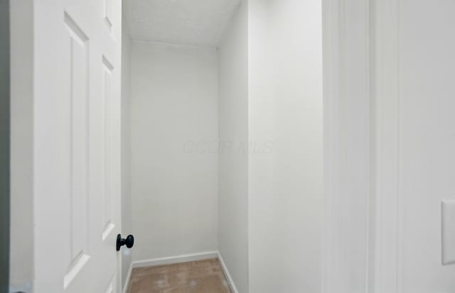 interior space with a textured ceiling, baseboards, and light colored carpet