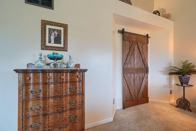 corridor featuring a barn door, visible vents, baseboards, and carpet floors