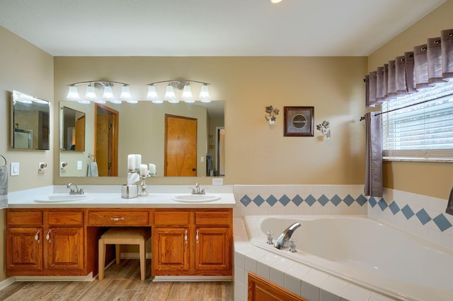 bathroom with double vanity, a garden tub, a sink, and wood finished floors