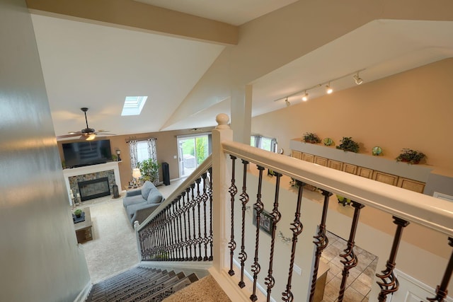 staircase featuring vaulted ceiling with skylight, a ceiling fan, a glass covered fireplace, and carpet floors