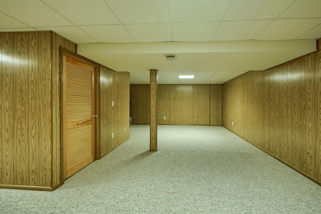 finished basement featuring wooden walls, carpet flooring, a paneled ceiling, and visible vents