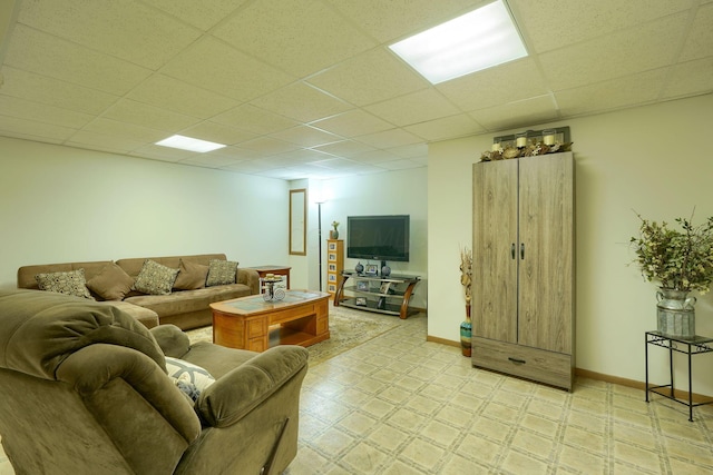 living area featuring a paneled ceiling, baseboards, and light floors