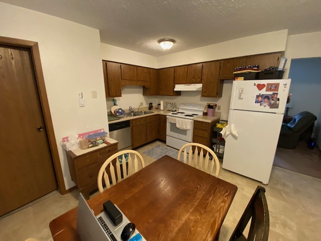 kitchen with white appliances, light countertops, a textured ceiling, under cabinet range hood, and a sink