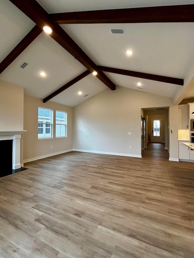 unfurnished living room with vaulted ceiling with beams, baseboards, light wood finished floors, and visible vents