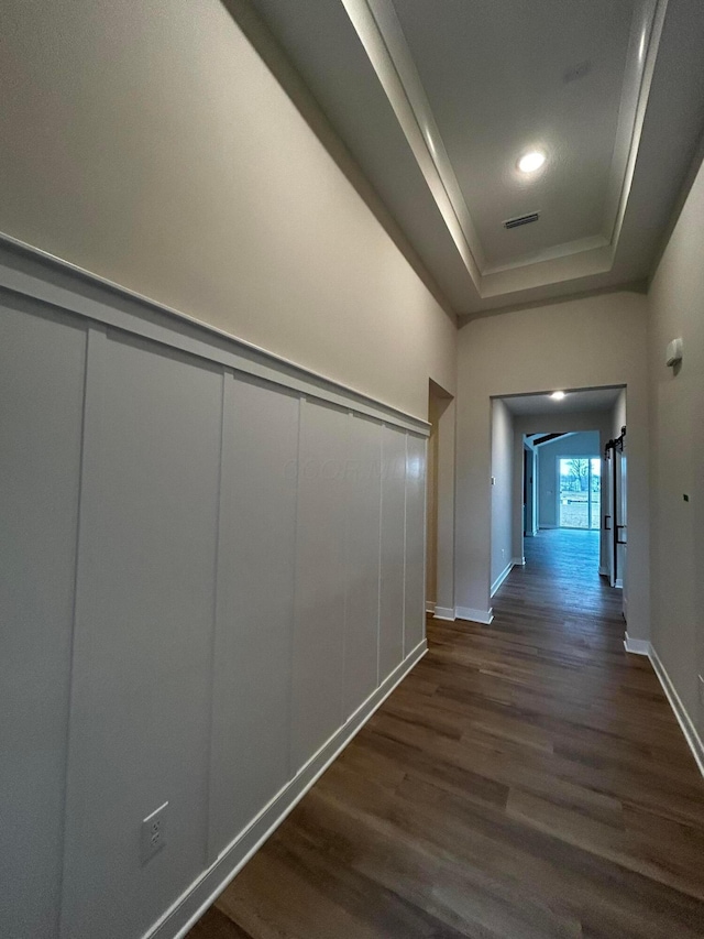 hallway with a decorative wall, visible vents, baseboards, dark wood finished floors, and a raised ceiling