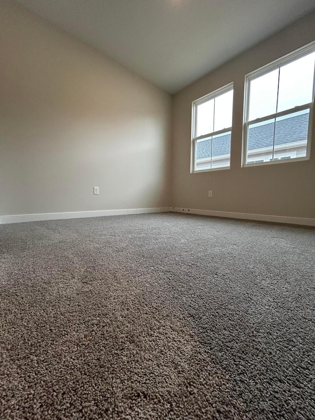 carpeted spare room featuring baseboards and vaulted ceiling