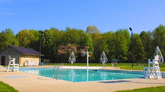 community pool with a patio area, fence, and a lawn