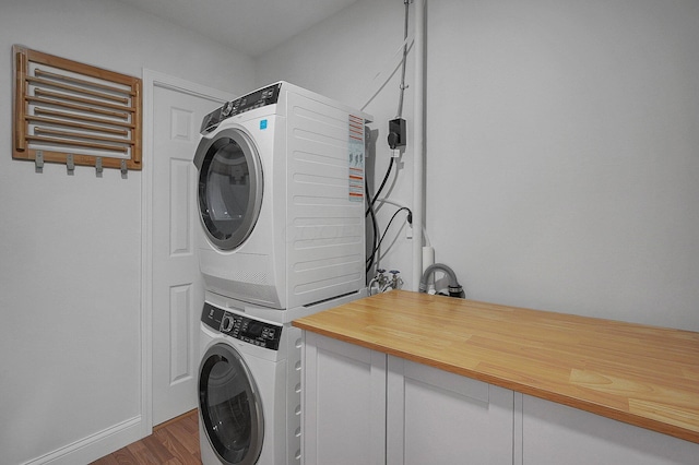 laundry room featuring dark wood-style flooring, stacked washer / drying machine, and laundry area