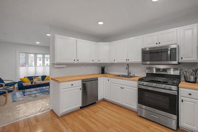kitchen featuring wood counters, white cabinetry, light wood-style flooring, a sink, and appliances with stainless steel finishes