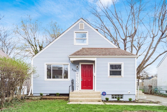 bungalow-style home featuring roof with shingles, a front yard, and fence