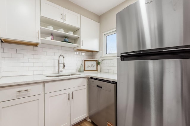 kitchen with backsplash, a sink, white cabinets, light stone countertops, and appliances with stainless steel finishes