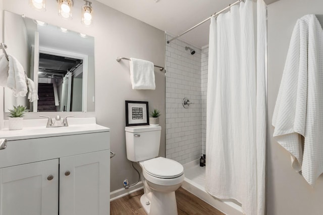 bathroom featuring baseboards, wood finished floors, toilet, vanity, and tiled shower