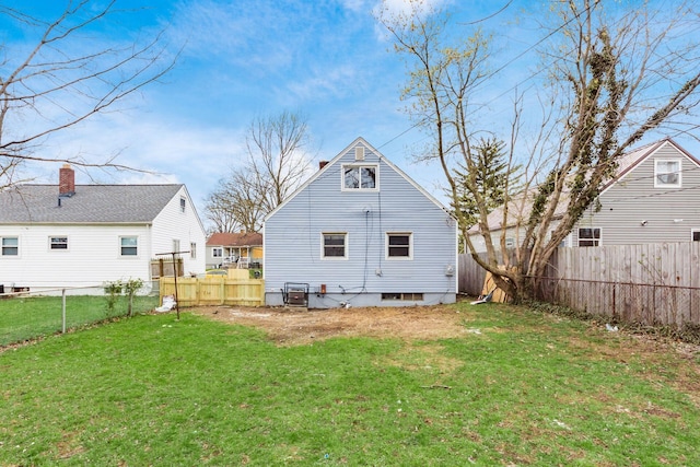 back of house featuring a fenced backyard, a chimney, and a lawn