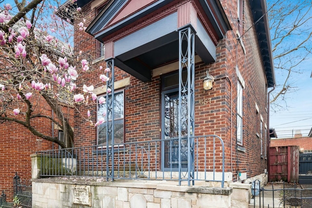 view of exterior entry featuring brick siding and fence
