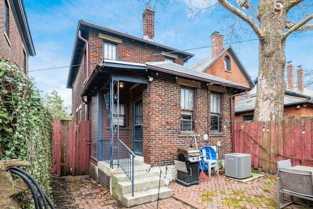 rear view of property with a patio, fence, brick siding, a chimney, and central AC unit