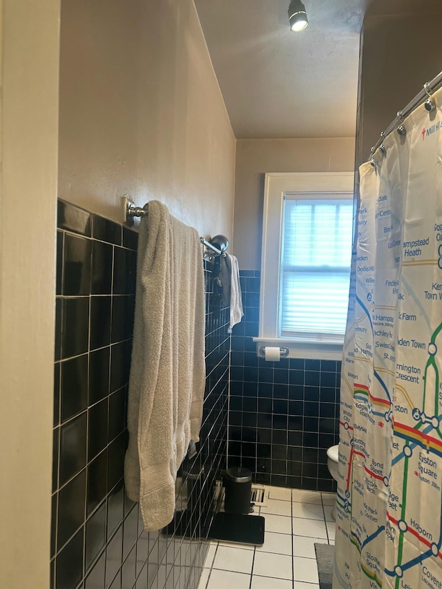bathroom featuring a shower with shower curtain, tile patterned floors, a wainscoted wall, toilet, and tile walls