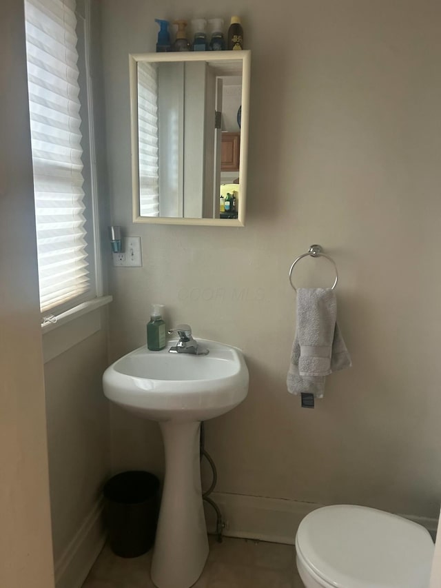 half bath featuring baseboards and toilet
