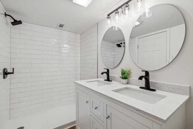 full bathroom with double vanity, a tile shower, visible vents, and a sink
