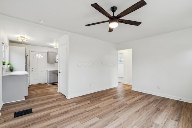 empty room with light wood-type flooring, a ceiling fan, baseboards, and visible vents