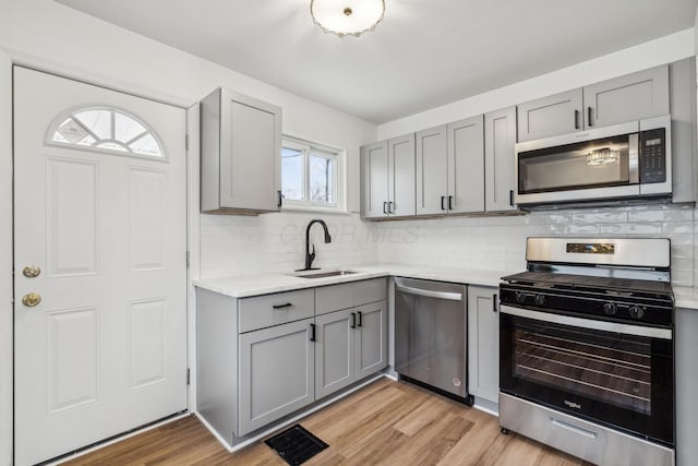 kitchen with gray cabinets, light countertops, a sink, light wood-style flooring, and stainless steel appliances