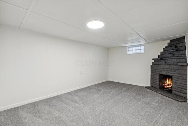 basement with carpet flooring, a stone fireplace, and baseboards