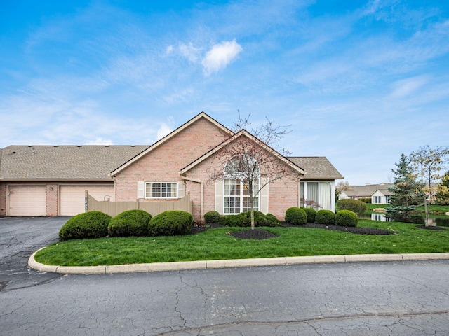 single story home featuring a front yard, a garage, aphalt driveway, brick siding, and roof with shingles