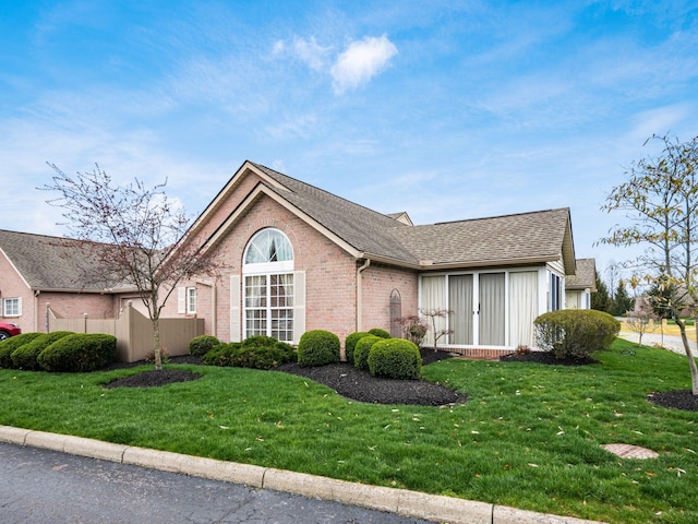 ranch-style house with roof with shingles, brick siding, fence, and a front lawn