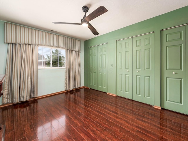 unfurnished bedroom with wood finished floors, ceiling fan, baseboards, and multiple closets