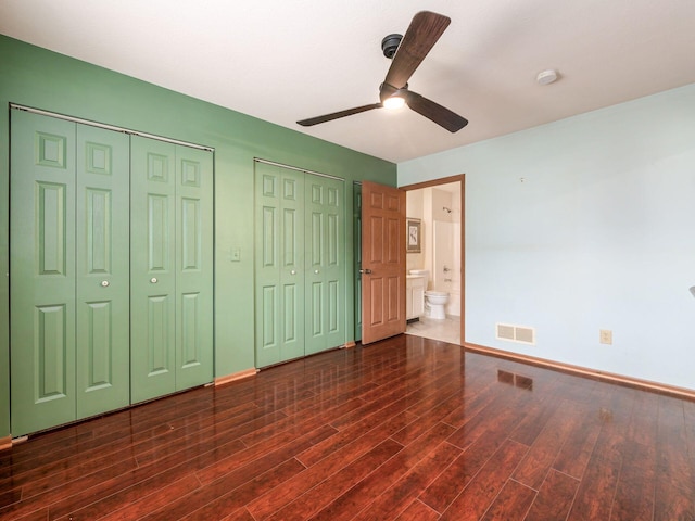 unfurnished bedroom with wood finished floors, baseboards, visible vents, and multiple closets