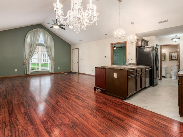 kitchen with pendant lighting, ceiling fan with notable chandelier, dark brown cabinets, a sink, and open floor plan