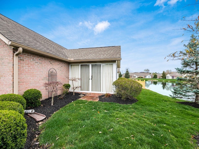 doorway to property with brick siding, a shingled roof, a yard, and a water view