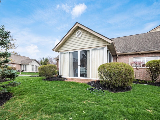 back of house with roof with shingles, a yard, and brick siding