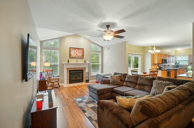 living room with a fireplace with flush hearth, ceiling fan with notable chandelier, lofted ceiling, and light wood-type flooring