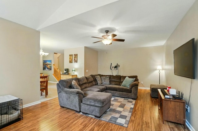 living room with ceiling fan with notable chandelier, wood finished floors, baseboards, and stairway
