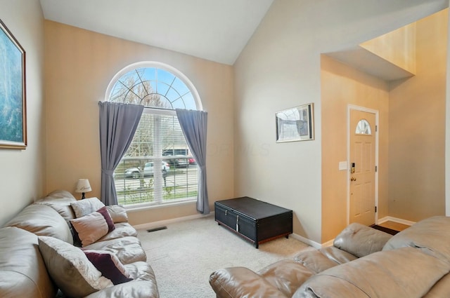 carpeted living area with high vaulted ceiling, baseboards, and visible vents