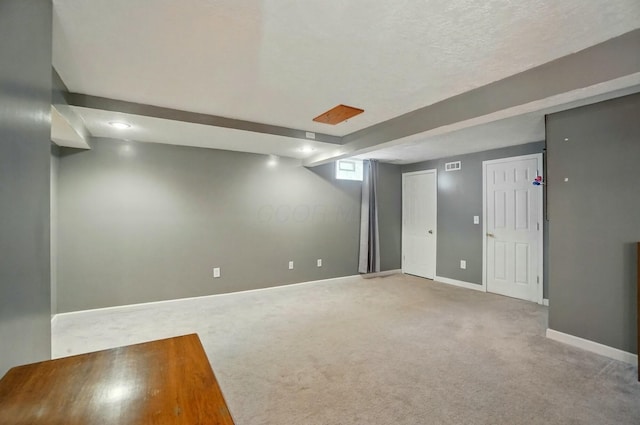 basement featuring baseboards, carpet flooring, a textured ceiling, and visible vents