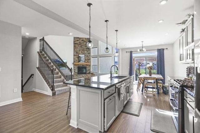 6003 Honey Farm Way, Grove City, OH 43123 - kitchen featuring dark wood-style flooring, a kitchen island with sink, a stone fireplace, appliances with stainless steel finishes, and a sink
