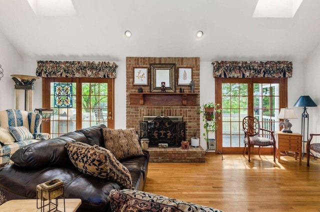 living area featuring lofted ceiling with skylight, a brick fireplace, recessed lighting, and light wood-type flooring
