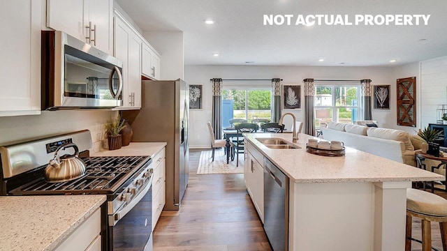 kitchen featuring an island with sink, white cabinetry, appliances with stainless steel finishes, a sink, and wood finished floors