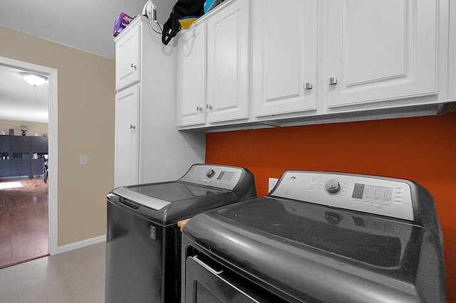 laundry area featuring light tile patterned floors, cabinet space, washing machine and dryer, and baseboards