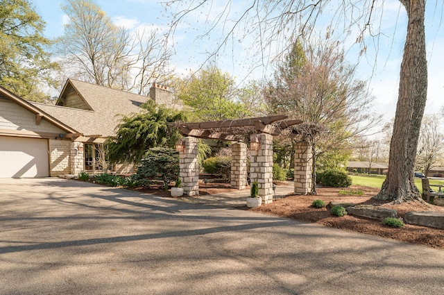 view of front of property featuring a chimney, a pergola, driveway, and a garage
