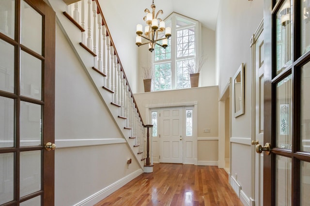 foyer entrance featuring stairs, a towering ceiling, wood finished floors, and a notable chandelier