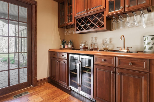 bar featuring beverage cooler, light wood finished floors, wet bar, visible vents, and a sink